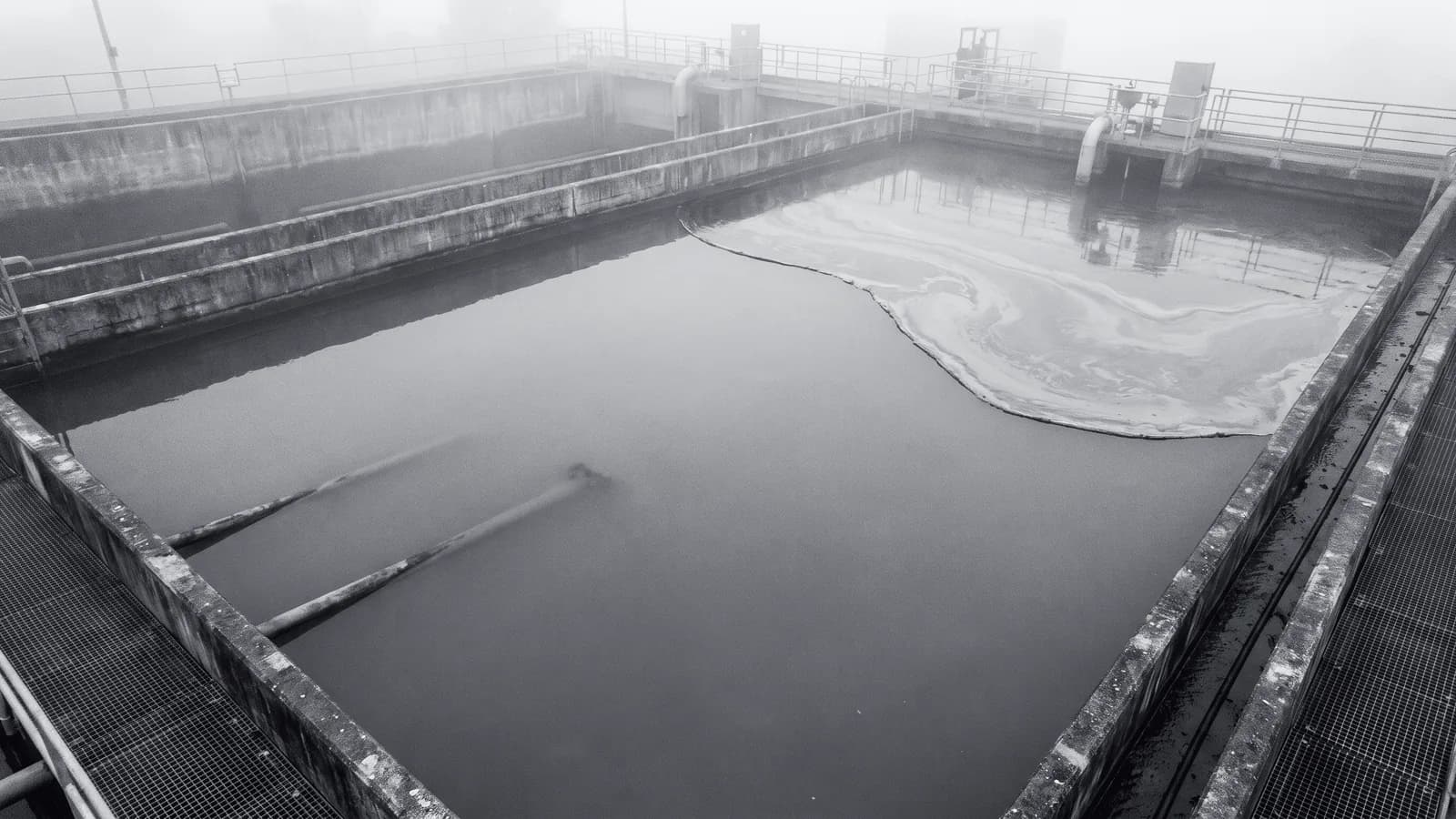 Illustrative frame: a settling tank seen from above, with computer vision segmenting an anomalous surface film against the clean water around it and reporting the share of the basin it covers. Shown in black and white, with the annotated regions revealed in colour.